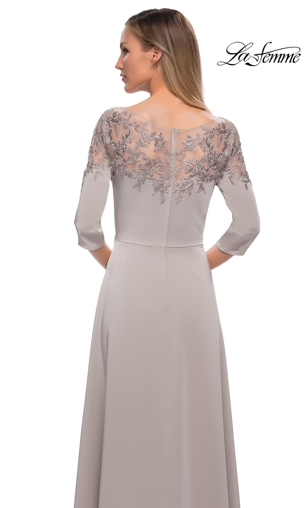 Woman in Long Formal Dress: La Femme 29227 in light gray, featuring sheer embroidered floral detail on the back and sleeves, facing away from the camera.